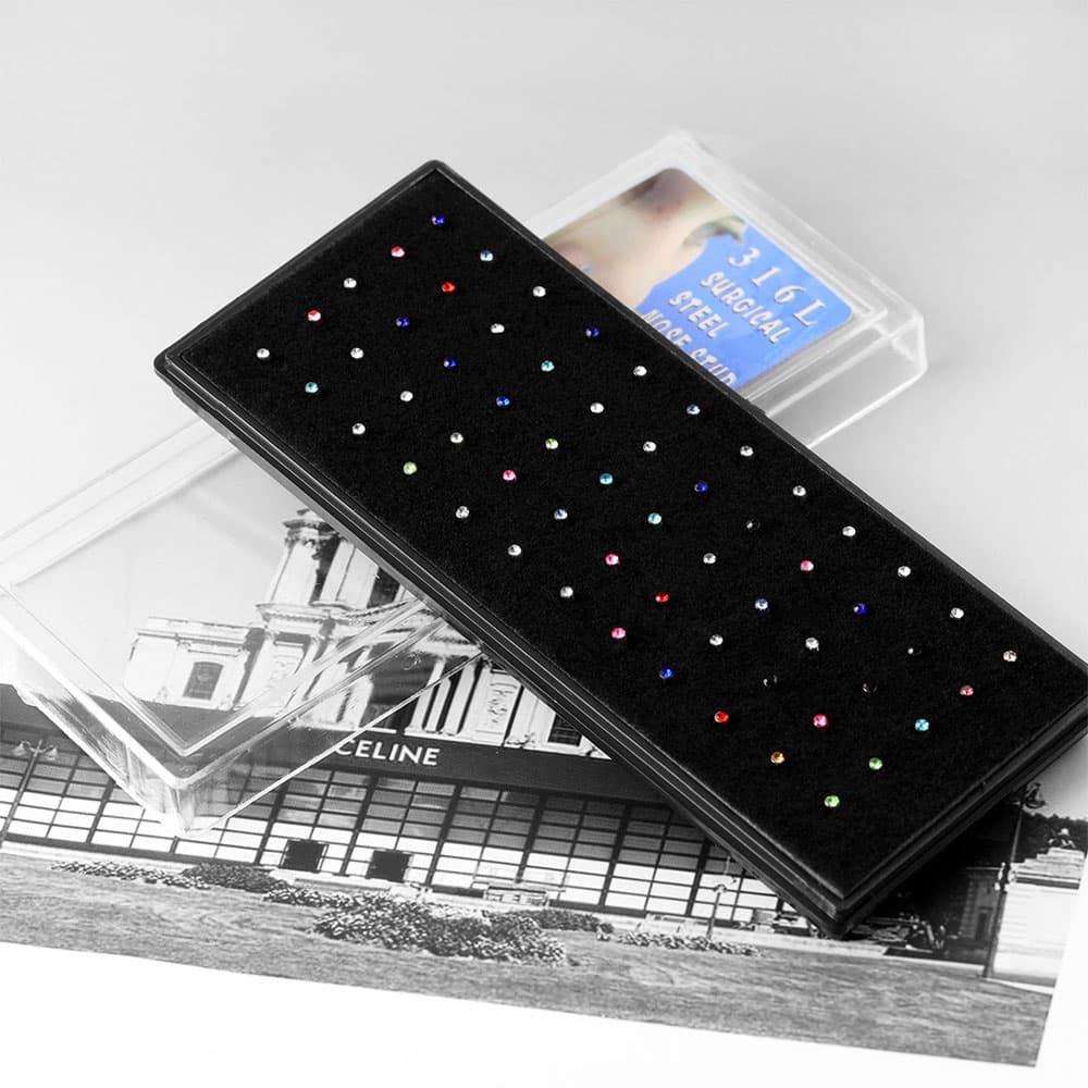 Angled view of a black 60-piece multi-color cubic zirconia nose stud jewelry tray pulled out of its clear plastic protective sleeve.
