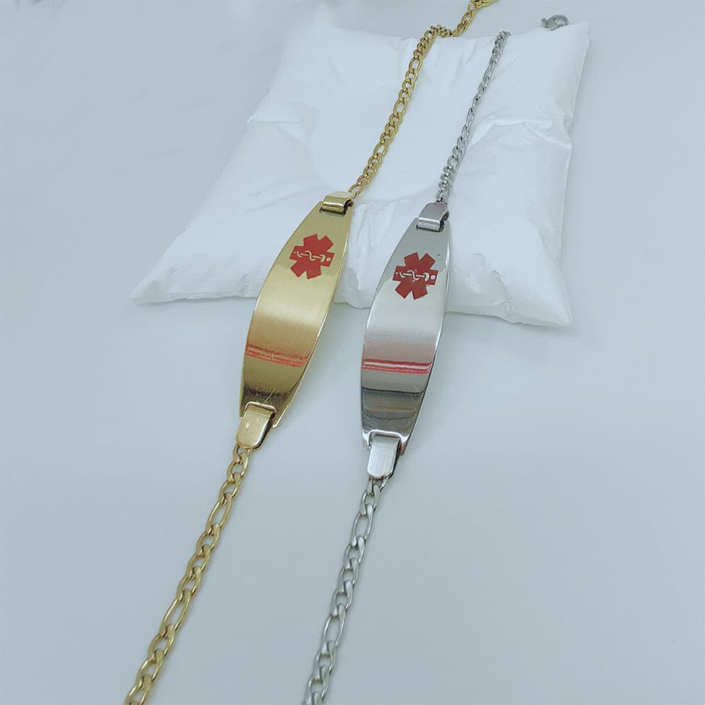 Gold and silver-tone stainless steel custom medical alert ID bracelets with Figaro chains displayed side-by-side on a white pillow.