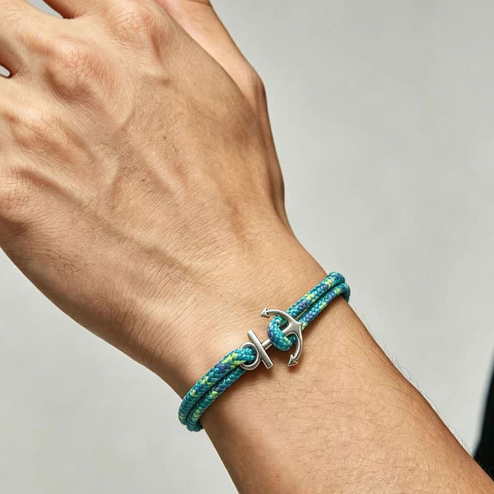 Close-up model shot of a man wearing a blue and green braided nautical rope bracelet with a silver stainless steel anchor hook.
