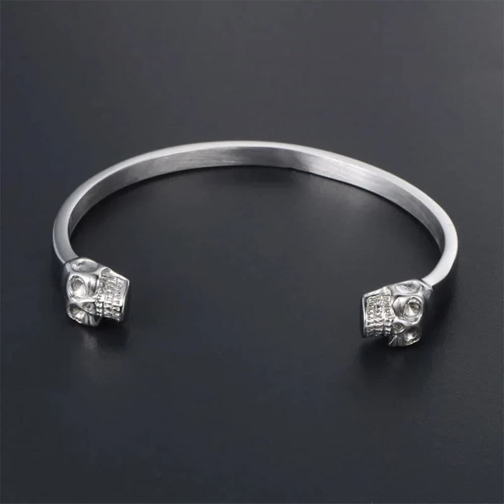 Silver stainless steel gothic double skull bangle cuff bracelet displayed on a dark background.